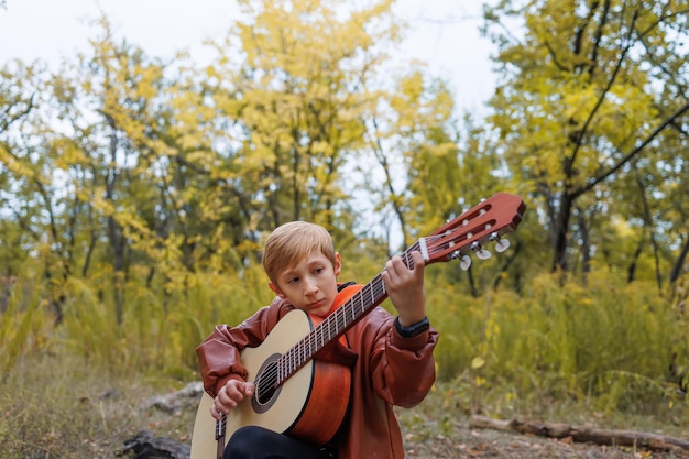 In autumn in the park a boy plays the guitar looks at the strings and tunes the guitar