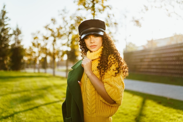 In the autumn park a girl in a leather cap and a bright yellow sweater slung over her shoulder a gre