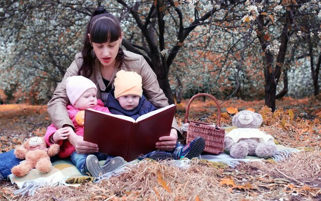 Осенний парк мама с близнецами на пледе на открытом воздухе в яблоневом саду