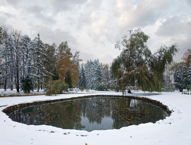 写真 秋の公園の池と最初の雪