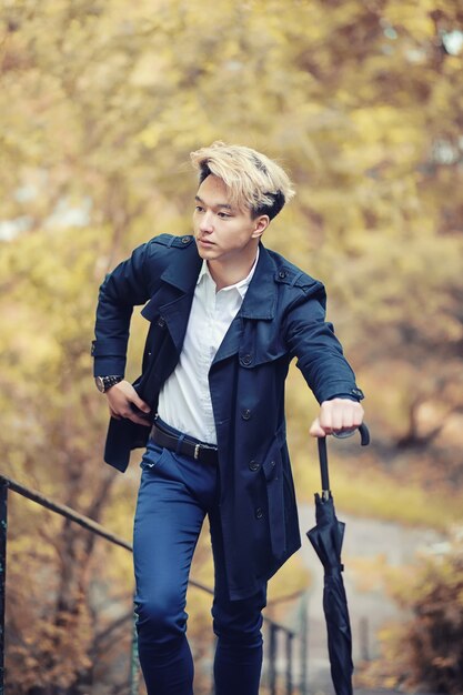 Autumn park in rainy weather and a young man with an\
umbrella