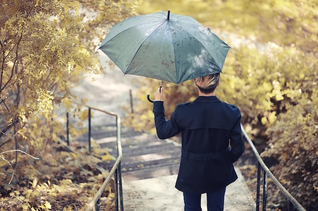 Autumn park in rainy weather and a young man with an\
umbrella