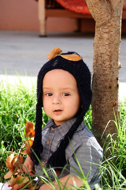 Autumn portrait of 2-3 years old child in garden. Fall season. Close-up view of cheerful sweet mixed-race baby boy in knitted cap