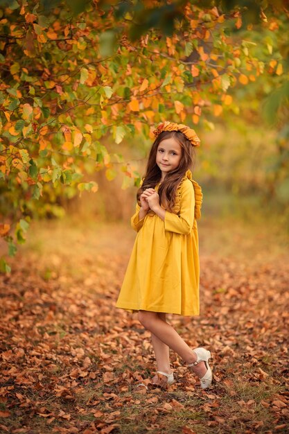 Autumn portrait of a beautiful girl walking in the park wearing a wreath of yellow leaves