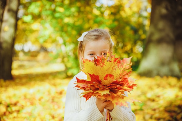 Autumn portrait of cute curly girl. Little funny girl playing with yellow leaves in the forest. Child in the autumn park. bouquet of autumn leaves