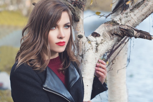 Autumn portrait of cute woman with healthy hair and makep walking in fall park outdoors