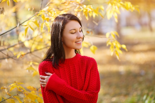 Autumn portrait of a young brunette girl woman in a red sweater