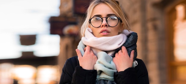 Autumn portrait of a young woman with glasses  she straightens her scarf she is very cold