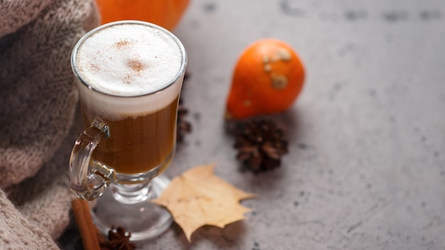 Autumn pumpkin latte glass. A warming drink and a knitted scarf on the gray table. 