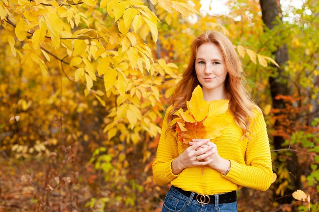 Autumn. red-haired girl in a yellow sweater holds a bouquet of autumn leaves in her hands. Warm tones. Orange. A place for text. High quality photo