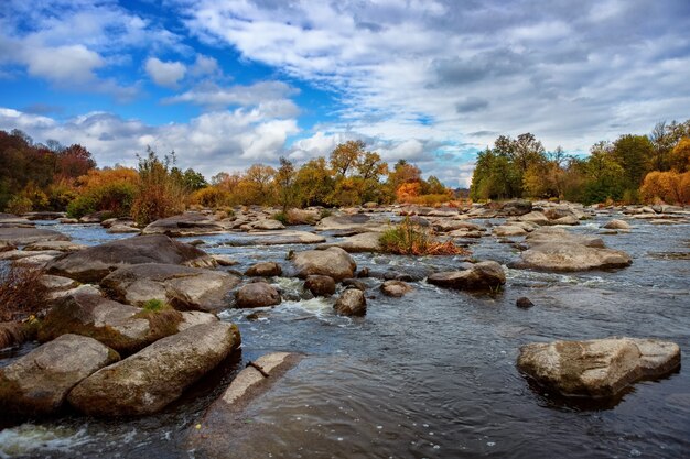 Осенняя река с красивыми большими камнями, голубым небом и деревьями