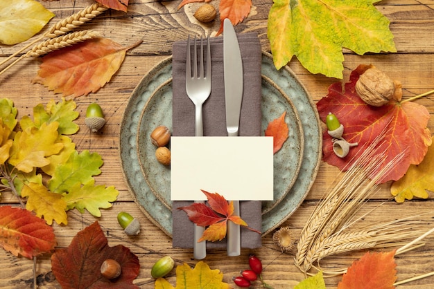 Autumn rustic table setting with blank place card between colorful leaves and berries top view mockup