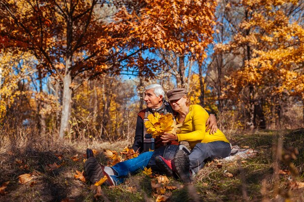 Autumn season fun. Senior couple hugging sitting in park. Man and woman relaxing outdoors