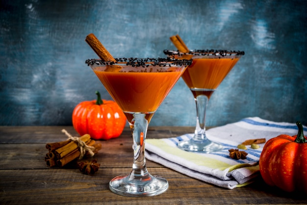 Autumn spicy pumpkin martini with cinnamon, anise stars and black sesame decoration, dark blue background