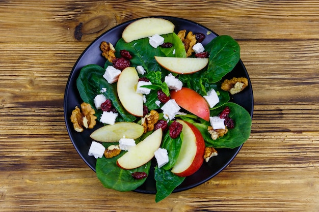 Autumn spinach salad with apple feta cheese walnut and dried cranberry on wooden table Top view Healthy vegetarian food