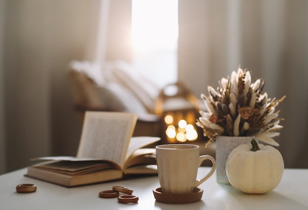 Natura morta autunnale e decorazioni per la casa in stile rustico con una tazza di libro di zucca e fiori