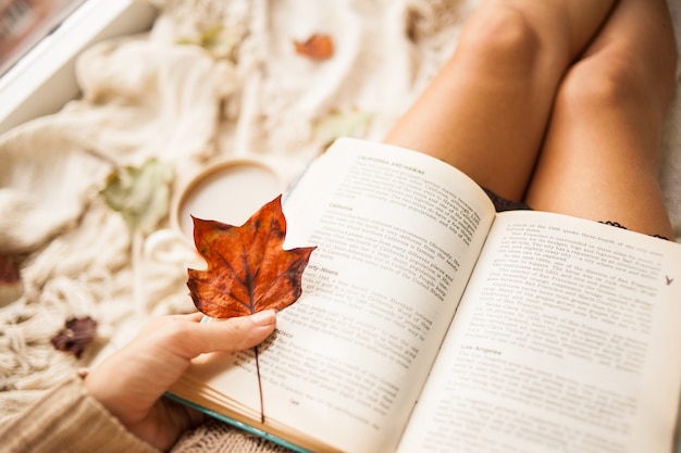 Photo autumn still life. view from above. the girl reads an open book while sitting on a plaid