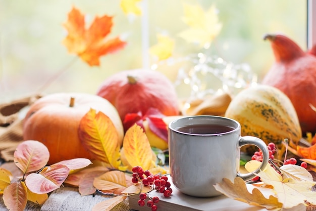 美しいボケ味の秋の静物。紅葉と熱い蒸しコーヒーまたは紅茶、オレンジ色のカボチャ季節、朝のコーヒー、日曜日の休息と静物の概念、モックアップレイアウト