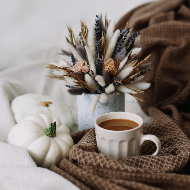 Autumn still life with a coffee cup with flowers and pumpkins on a cozy plaid
