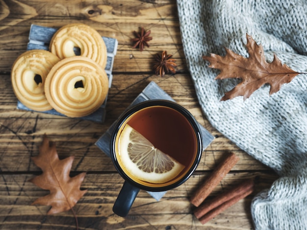 Autumn still life with cup of tea, cookies, sweater and leaves on wooden table.