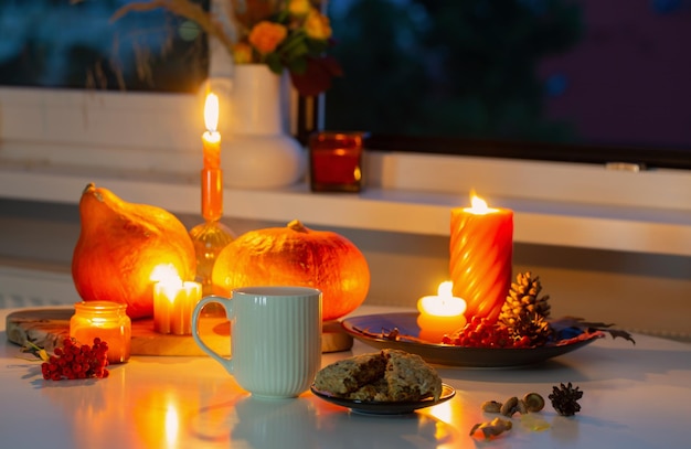 осенний натюрморт с тыквами, горящими свечами и чашкой чая