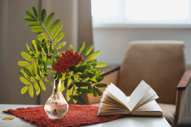 Autumn still life with a rowan branch in a vase and a book and apples in a cozy home interior