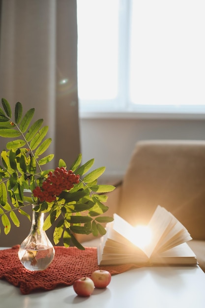 Autumn still life with a rowan branch in a vase book and apples in a cozy home interior