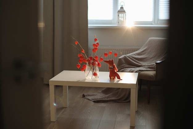 Осенний натюрморт с игрушечной лисицей, цветы веточки красного физалиса в вазе в уютном домашнем интерьере