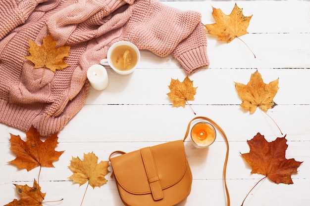 Autunno natura morta, foglie gialle, zucca, candele, maglione lavorato a maglia su una vista bianca e dall'alto.