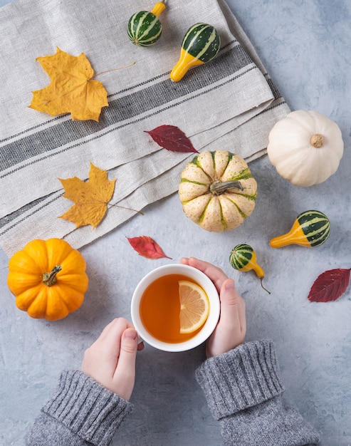 Autumn stillife. cup of tea in hand and some decorative pumpkins and leaves on blue.