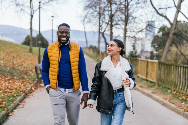 秋の散歩 落ち葉のある公園でカメラに向かって歩いている笑顔の黒人少年と白人少女のカジュアルなライフ スタイル ショット
