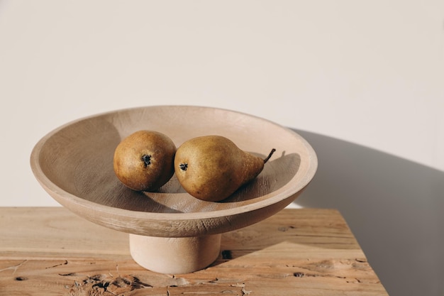 Autumn summer fruit food still life Couple of yellow pears wooden bowl on table in sunset light Blurred beige wall background long shadows Selective focus Rustic farm composition