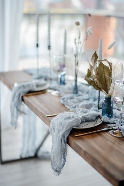 Autumn table decoration, wooden table served with dried flower, white plate, vintage cutlery, candeles with bright blue gauze tablecloth. Top view, selective focus.