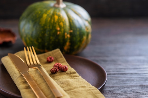 Autumn table settings fresh pumpkin and gold cutlery with linen napkin on wooden plate