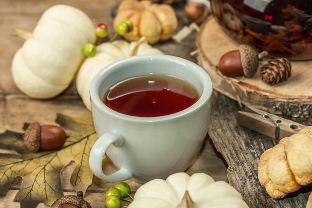 Autumn tea concept. Cookies with pumpkin puree, black tea in a glass teapot, fall decor. Wreath, candles, a cozy sweater. Old wooden background, close up