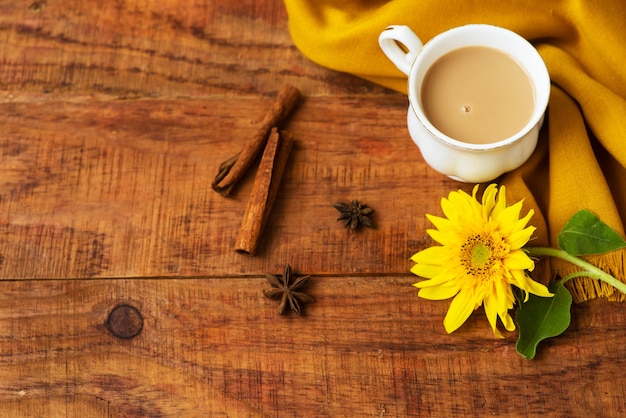 Autumn tea cup composition with milk, yellow scarfs, cinnamon sticks and sunflower on a wooden background Autumn background. Warm, cozy atmosphere of autumn. Flat lay, layout. Place for text, frame