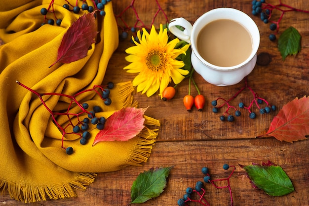 Composizione nella tazza da tè autunnale, sciarpa gialla, bacche di rosa e fiore di girasole su uno sfondo di legno