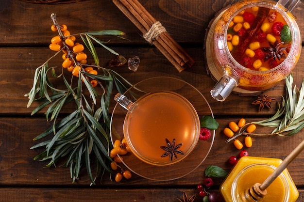 Фото Осенний чай с ягодами и медом. облепиха и малина в стеклянном чайнике, чашки с налитым