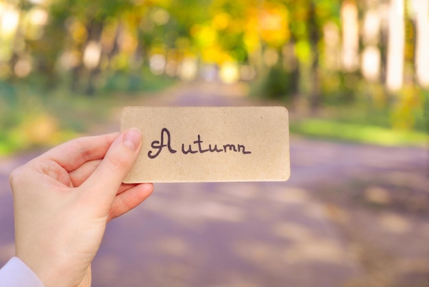 Autumn text on a card Girl holding card in autumn park in sunny rays