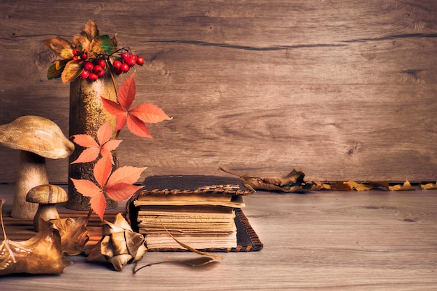 木製のキノコと秋の感謝祭の配置。秋の葉、リンゴ、ピーマン、栗。秋の静物アレンジメント室内、古い木製のテーブル、コピースペースに古いアンティークの本。