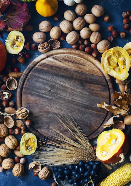 Autumn or thanksgiving background with decorative pumpkin corn nuts grapes wheat and wooden board with copy space on dark stone table harvest still life composition with space for text