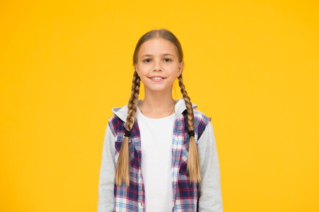 Autumn time hipster girl yellow background happy school girl casual style kid fashion child cute blond hair childhood happiness happy childrens day small girl checkered jacket