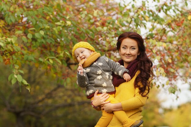 Autumn time. Portrait of charming mother with her little daughter with apple in arms in sunny warm autumn park during walk, copyspace