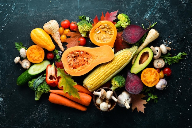 Autumn vegetables on a black stone background Pumpkin tomatoes corn cucumber onion carrot Autumn food Top view Free copy space