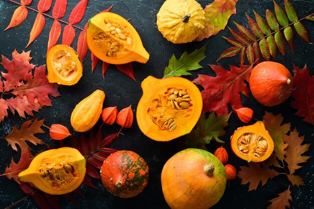 Autumn vegetables Pumpkin with pumpkin seeds and autumn leaves flat lay On a black stone background Top view Free space for your text