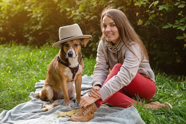 ペットと一緒に秋の散歩。帽子をかぶった犬を持つ女性は格子縞に座っています。