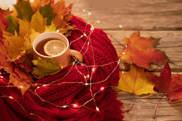 Autumn warm composition in red tones on a wooden background with a cup of tea, garland.