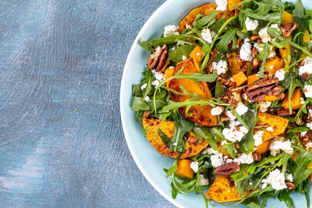 Autumn warm salad Homemade fall season salad with grill and baked pumpkin arugula feta cheese and crushed nuts Whole vegan paleo fruit and vegetable salad idea