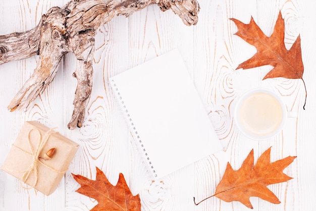 Autumn or winter composition with a blank diary a cup of coffee autumn dry leaves driftwood on a rustic whitewashed wooden background Flat lay copy space