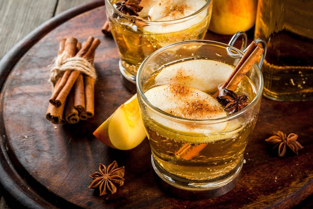 Autumn and winter drinks. Traditional home-made apple cider, cocktail of cider with aromatic spices - cinnamon and anise. On an old wooden rustic table, on a tray. copyspace